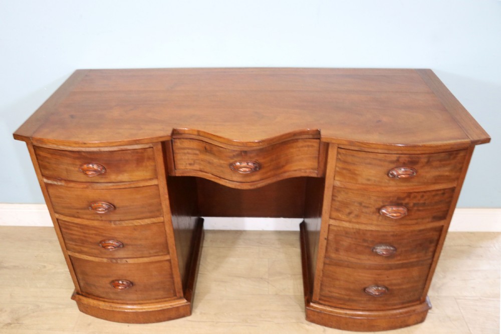 A late Victorian mahogany twin pedestal desk featuring a curved front structure and nine drawers with turned wooden handles.
