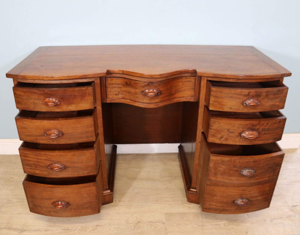 A late Victorian mahogany twin pedestal desk featuring a curved front structure and nine drawers with turned wooden handles. View II