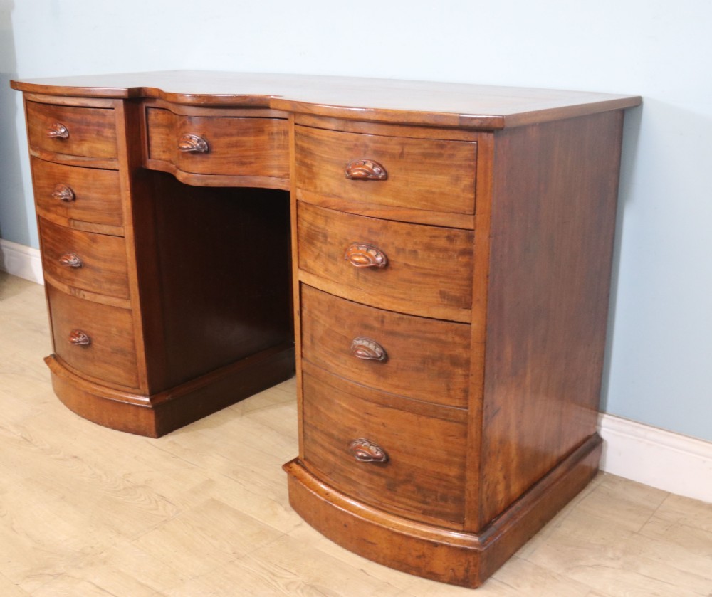 A late Victorian mahogany twin pedestal desk featuring a curved front structure and nine drawers with turned wooden handles. View V