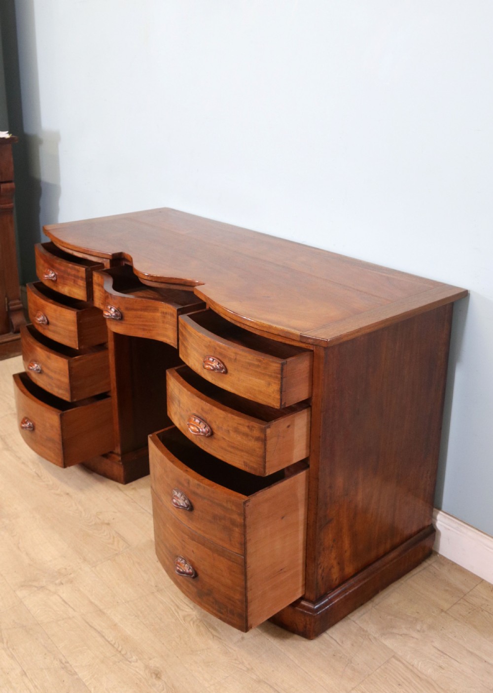 A late Victorian mahogany twin pedestal desk featuring a curved front structure and nine drawers with turned wooden handles. View VI