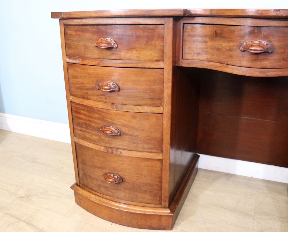 A late Victorian mahogany twin pedestal desk featuring a curved front structure and nine drawers with turned wooden handles. View X