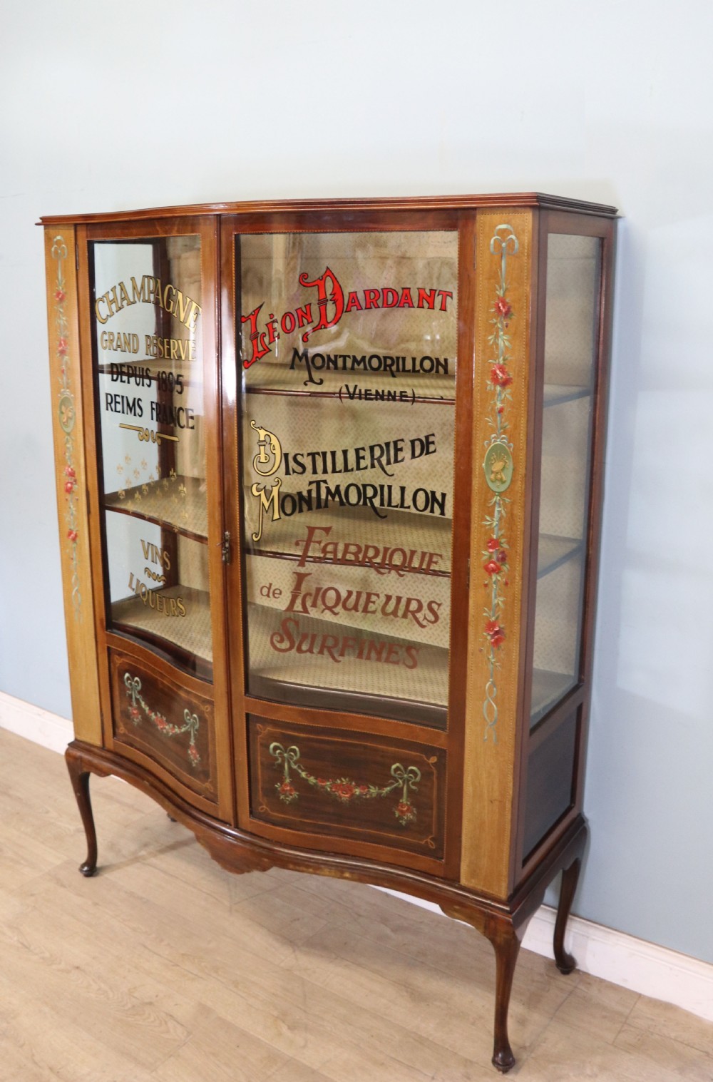 An Edwardian mahogany and satinwood display cabinet featuring curved glass doors decorated with French text and painted floral motifs, resting on slender cabriole legs. View III
