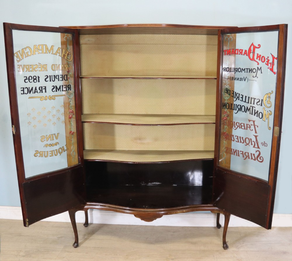 An Edwardian mahogany and satinwood display cabinet featuring curved glass doors decorated with French text and painted floral motifs, resting on slender cabriole legs. View V