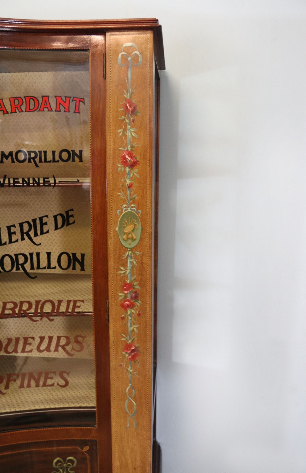 An Edwardian mahogany and satinwood display cabinet featuring curved glass doors decorated with French text and painted floral motifs, resting on slender cabriole legs. View VIII