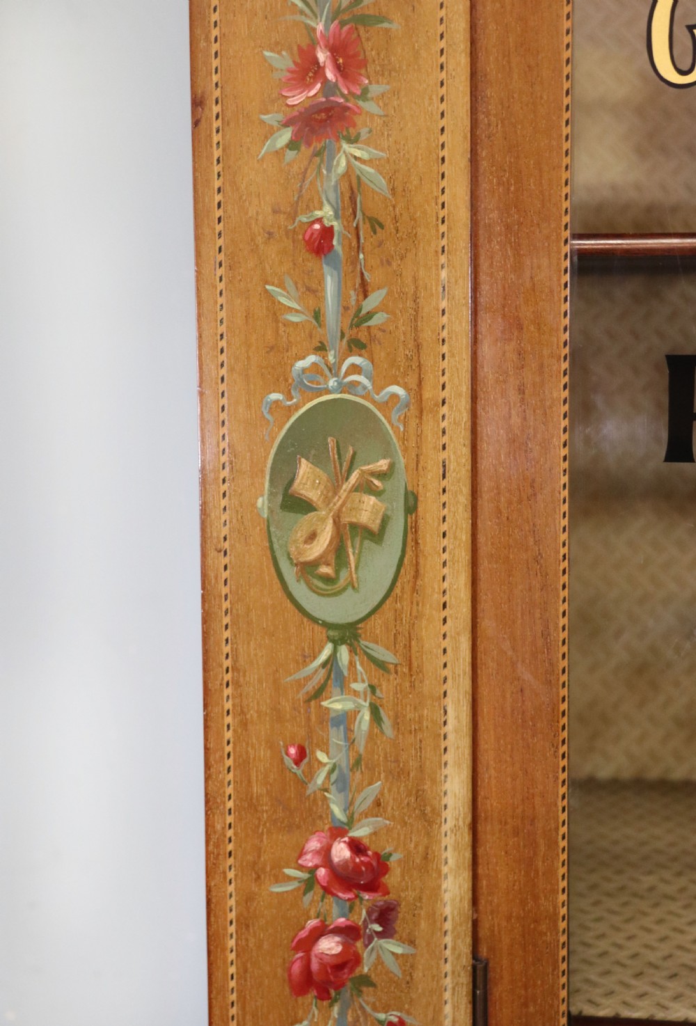 An Edwardian mahogany and satinwood display cabinet featuring curved glass doors decorated with French text and painted floral motifs, resting on slender cabriole legs. View IX