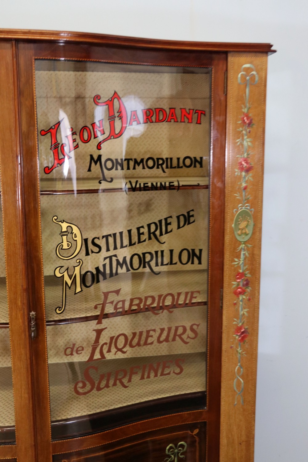 An Edwardian mahogany and satinwood display cabinet featuring curved glass doors decorated with French text and painted floral motifs, resting on slender cabriole legs. View XI