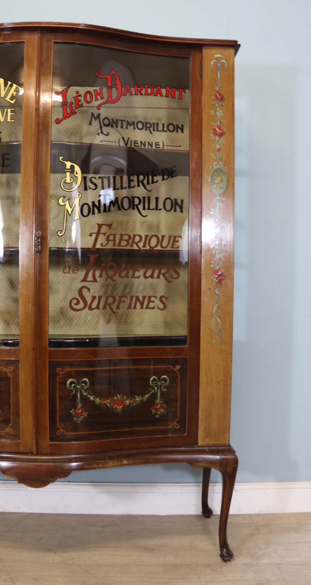 An Edwardian mahogany and satinwood display cabinet featuring curved glass doors decorated with French text and painted floral motifs, resting on slender cabriole legs. View XIII