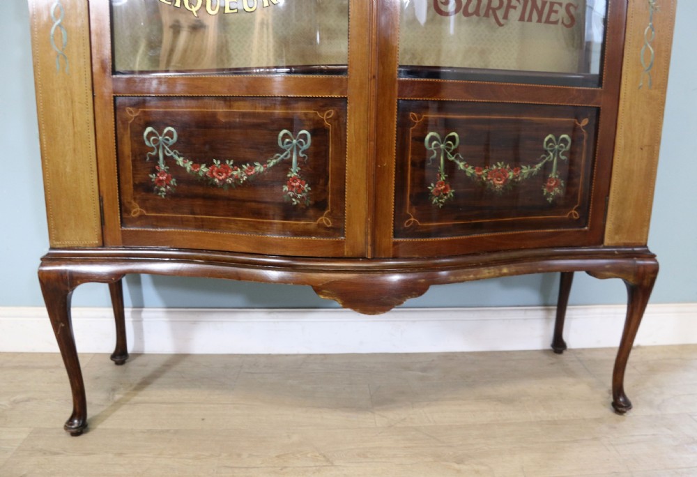 An Edwardian mahogany and satinwood display cabinet featuring curved glass doors decorated with French text and painted floral motifs, resting on slender cabriole legs. View XXV