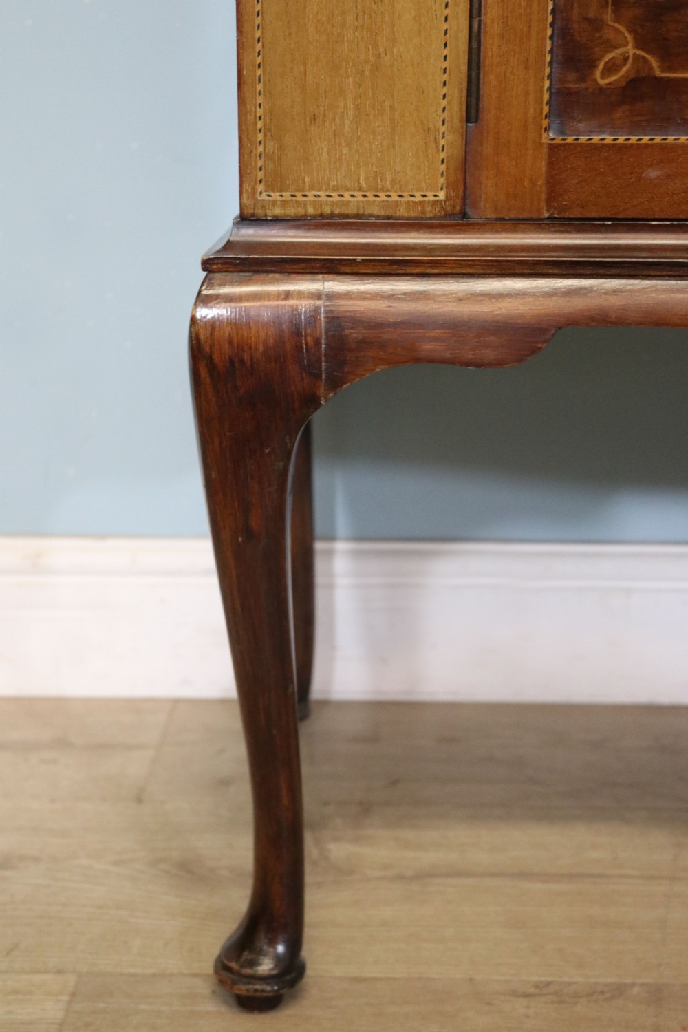 An Edwardian mahogany and satinwood display cabinet featuring curved glass doors decorated with French text and painted floral motifs, resting on slender cabriole legs. View XXX
