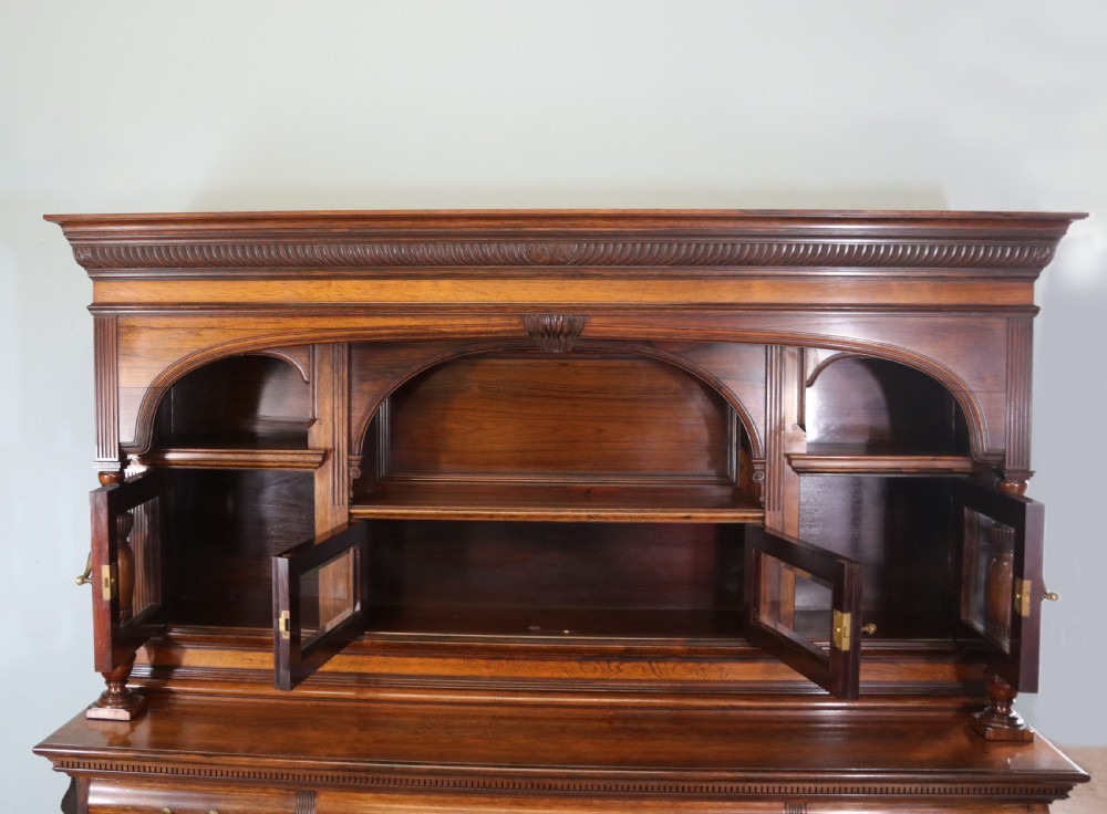 A large Victorian rosewood sideboard featuring an upper tier with arched alcoves, mirrors, and glazed cabinets over a lower base with drawers and panelled doors. View VI