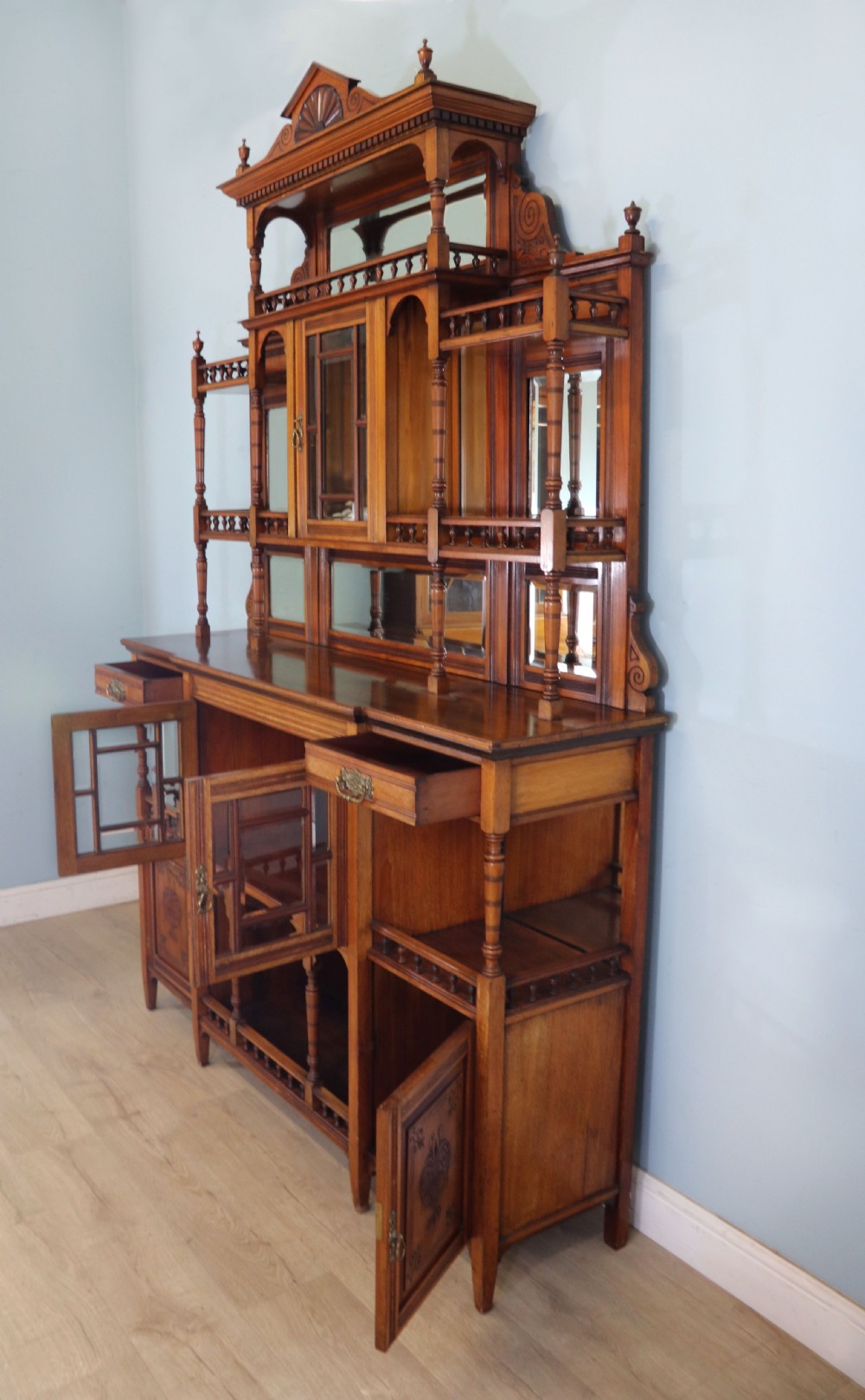 A late Victorian carved wood side cabinet featuring an ornate upper tier with multiple bevelled mirror plates, spindled galleries, glass-front doors, and carved lower cupboards. View VI