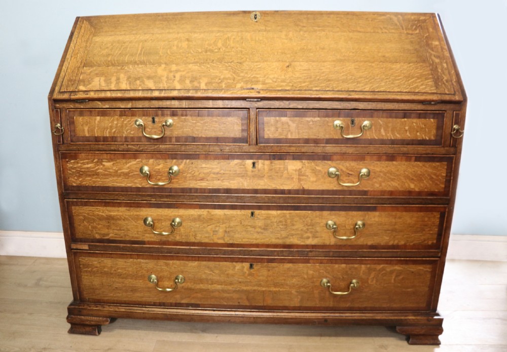 An open George III oak bureau featuring mahogany crossbanding, brass swan-neck handles, pull-out lopers, and a fitted interior with pigeonholes. View II