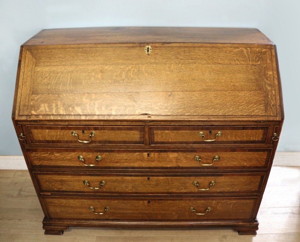 An open George III oak bureau featuring mahogany crossbanding, brass swan-neck handles, pull-out lopers, and a fitted interior with pigeonholes. View III