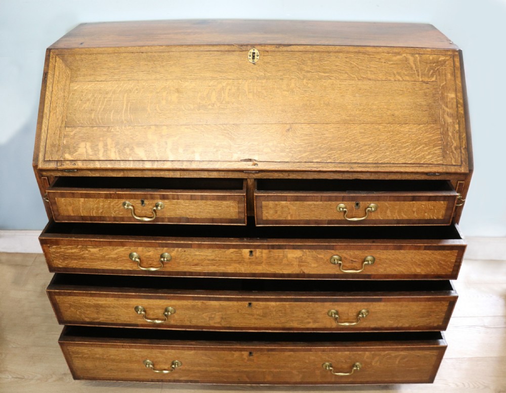 An open George III oak bureau featuring mahogany crossbanding, brass swan-neck handles, pull-out lopers, and a fitted interior with pigeonholes. View IV
