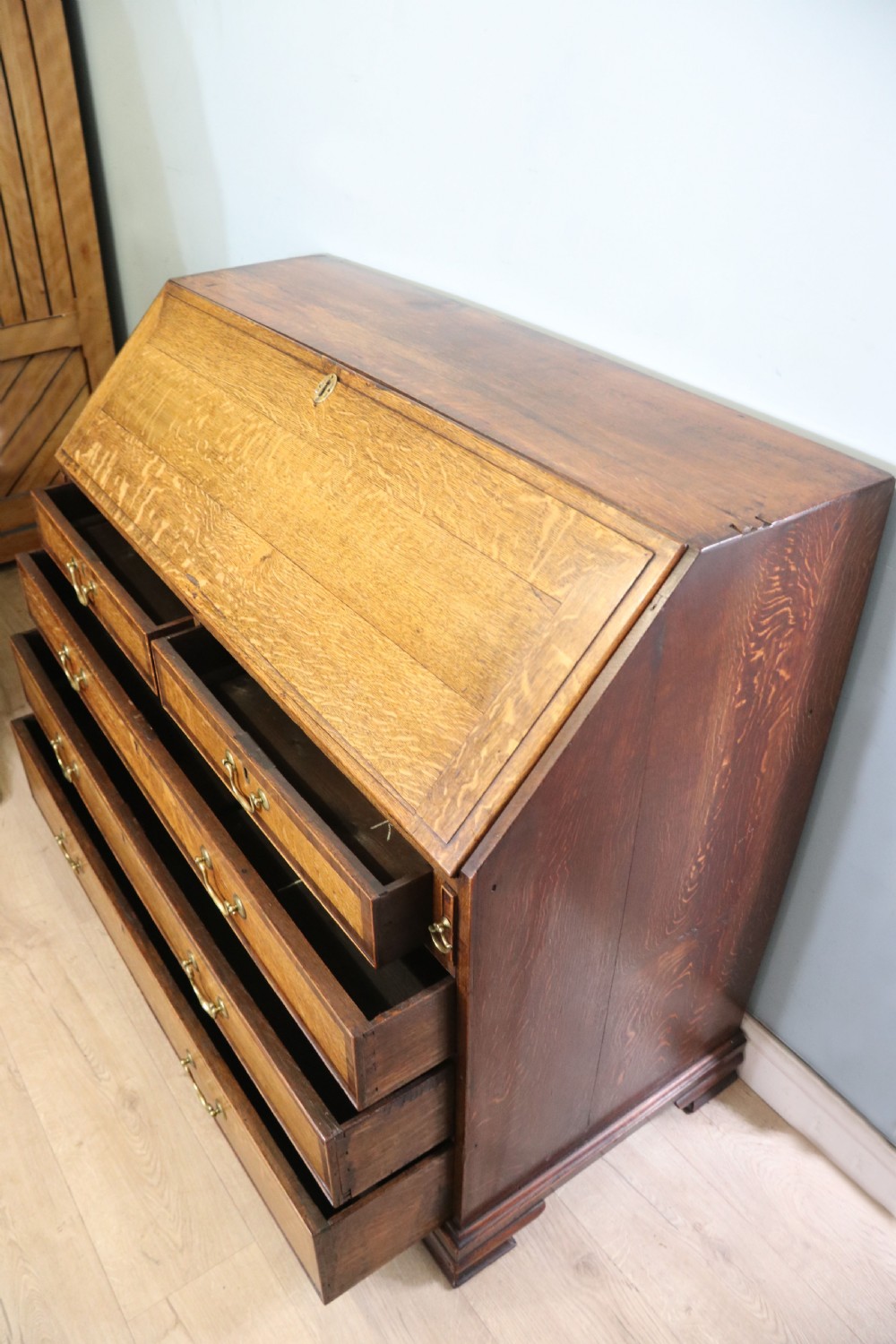 An open George III oak bureau featuring mahogany crossbanding, brass swan-neck handles, pull-out lopers, and a fitted interior with pigeonholes. View V
