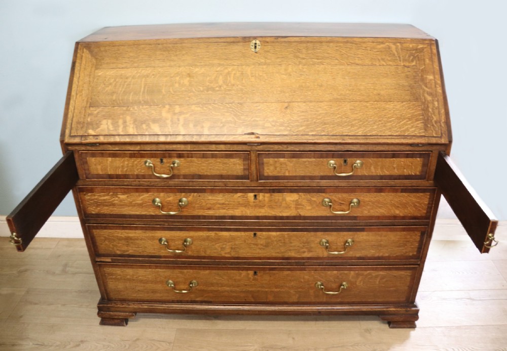 An open George III oak bureau featuring mahogany crossbanding, brass swan-neck handles, pull-out lopers, and a fitted interior with pigeonholes. View VI
