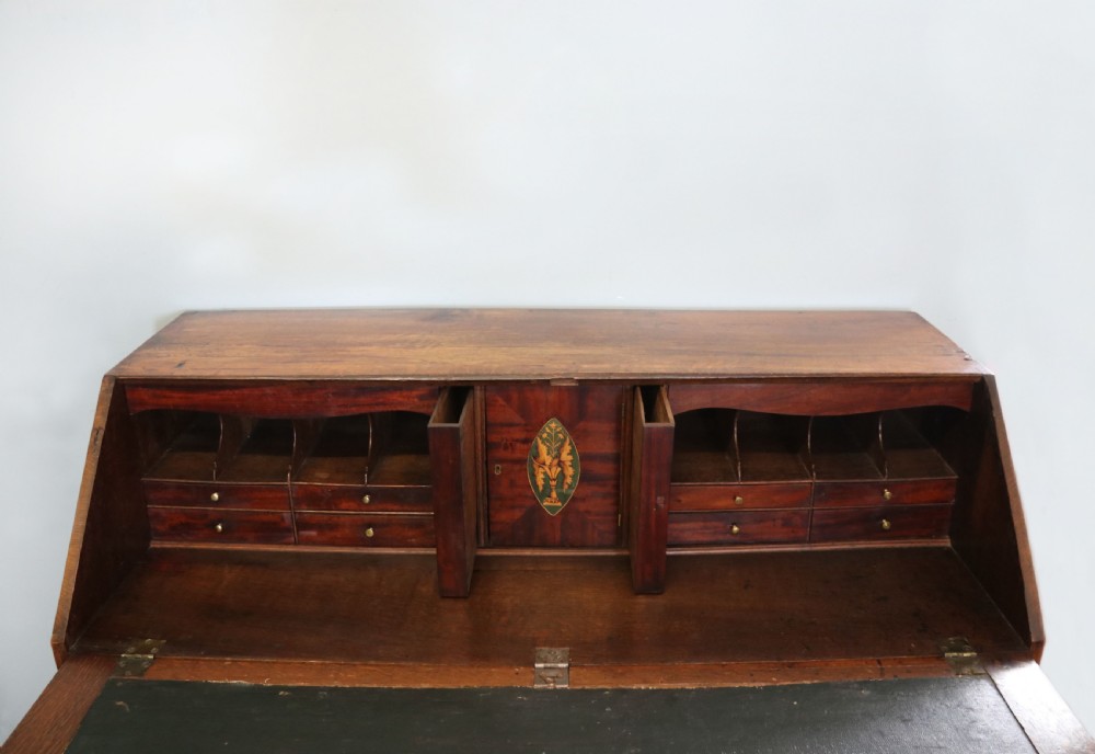 An open George III oak bureau featuring mahogany crossbanding, brass swan-neck handles, pull-out lopers, and a fitted interior with pigeonholes. View VII