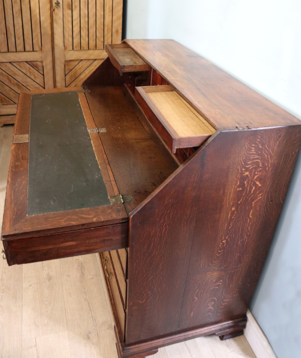 An open George III oak bureau featuring mahogany crossbanding, brass swan-neck handles, pull-out lopers, and a fitted interior with pigeonholes. View XII
