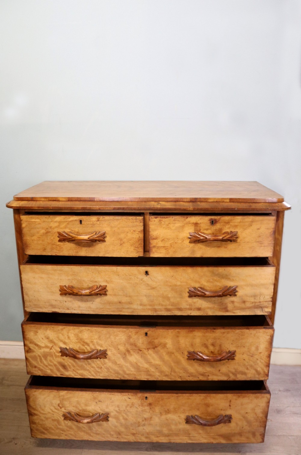 A Victorian light wood chest of drawers with two short drawers over three long drawers, featuring carved leaf handles and a solid plinth base. View II