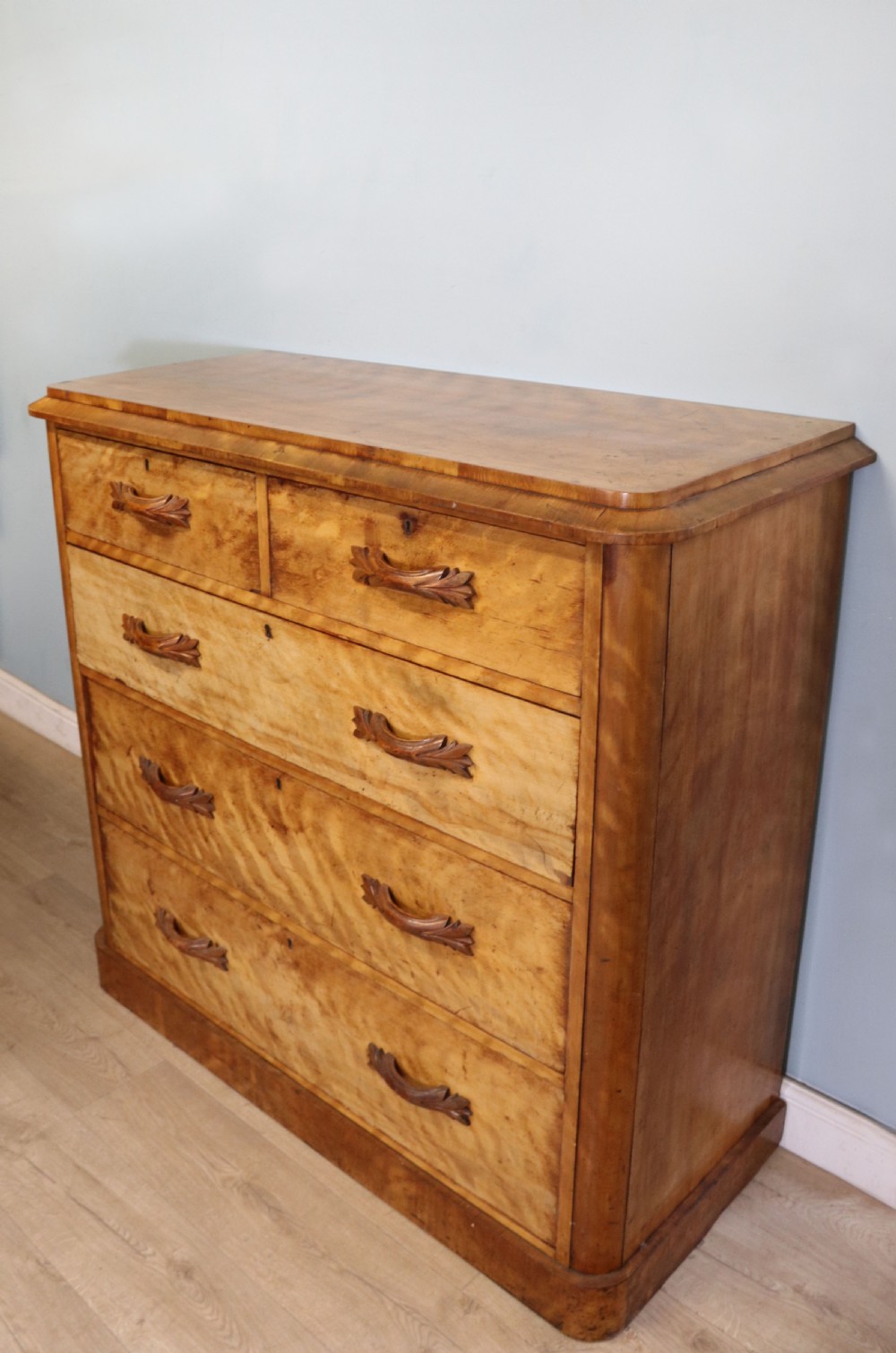 A Victorian light wood chest of drawers with two short drawers over three long drawers, featuring carved leaf handles and a solid plinth base. View III
