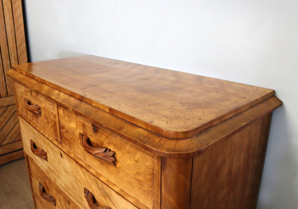 A Victorian light wood chest of drawers with two short drawers over three long drawers, featuring carved leaf handles and a solid plinth base. View V