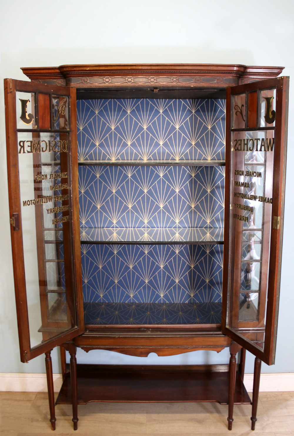 A tall mahogany glazed display cabinet featuring two central glass doors, glazed sides, turned legs, a lower undertier shelf, and gilded gold lettering inside. View II