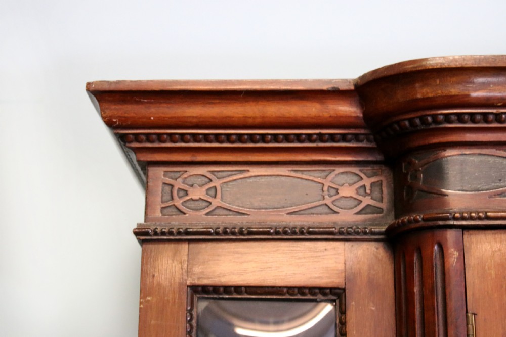 A tall mahogany glazed display cabinet featuring two central glass doors, glazed sides, turned legs, a lower undertier shelf, and gilded gold lettering inside. View V