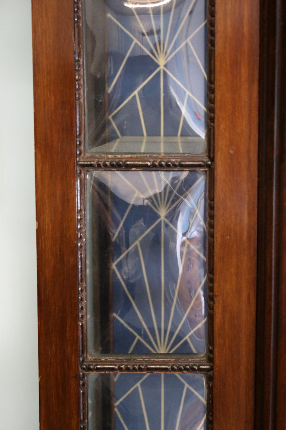 A tall mahogany glazed display cabinet featuring two central glass doors, glazed sides, turned legs, a lower undertier shelf, and gilded gold lettering inside. View VII