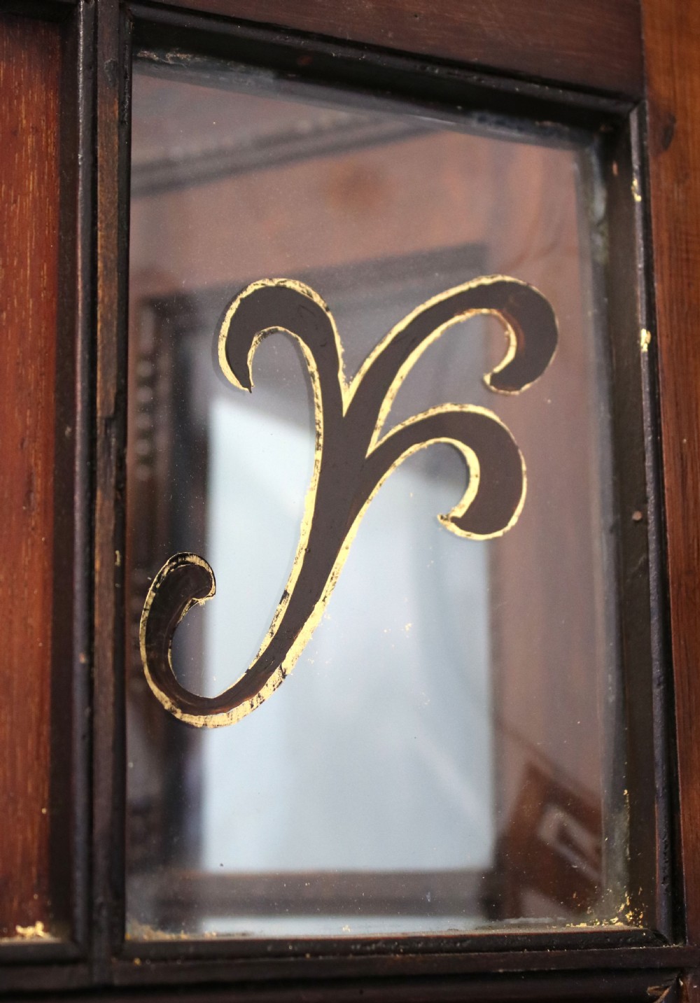 A tall mahogany glazed display cabinet featuring two central glass doors, glazed sides, turned legs, a lower undertier shelf, and gilded gold lettering inside. View X