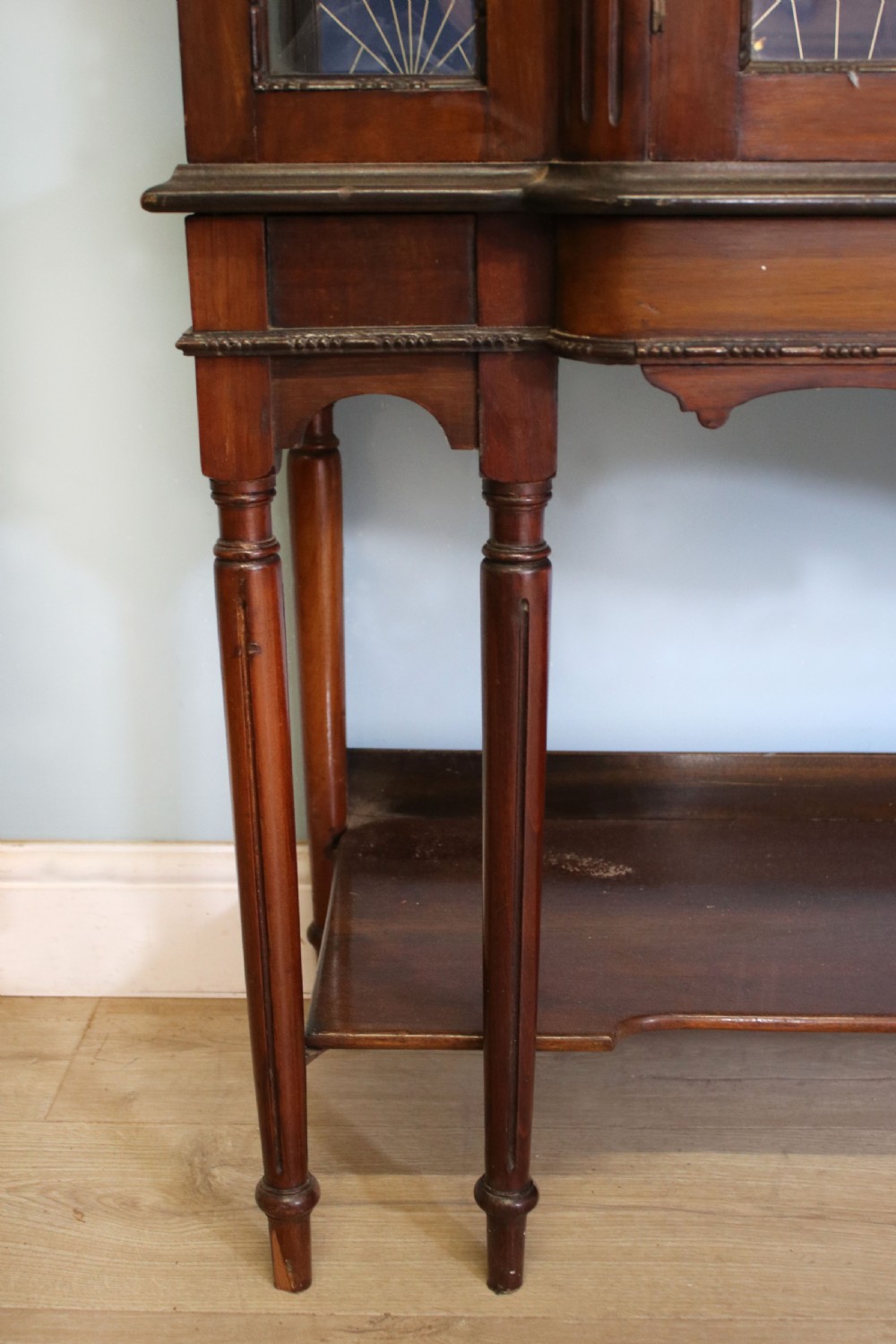 A tall mahogany glazed display cabinet featuring two central glass doors, glazed sides, turned legs, a lower undertier shelf, and gilded gold lettering inside. View XIII