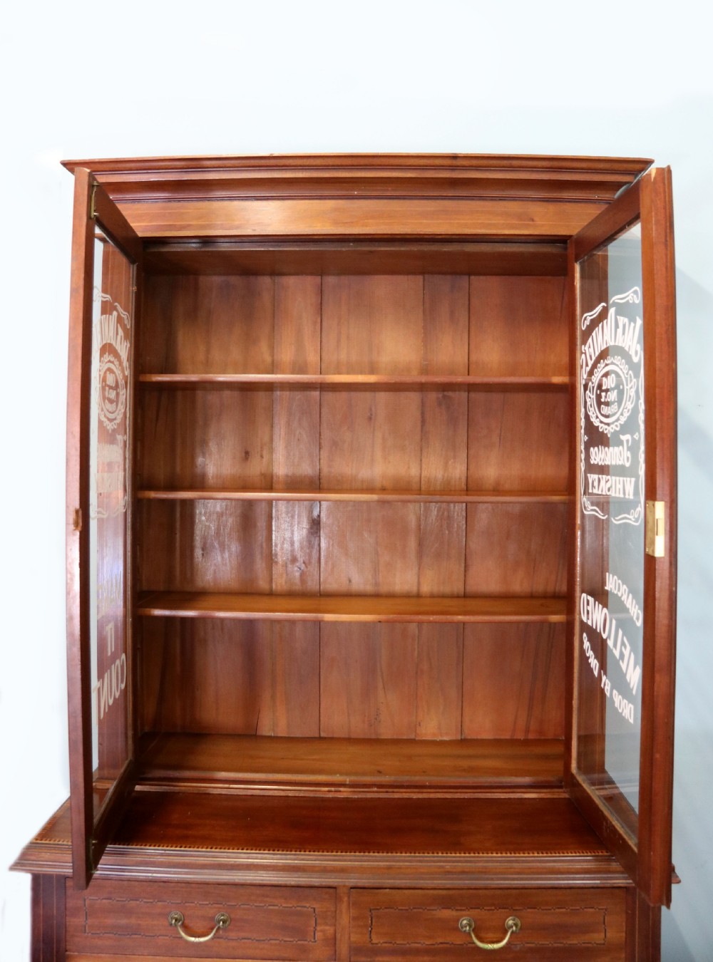 A late Victorian warm brown wooden cabinet featuring a glazed upper display section with white Jack Daniels typography and two lower panelled doors. View VIII
