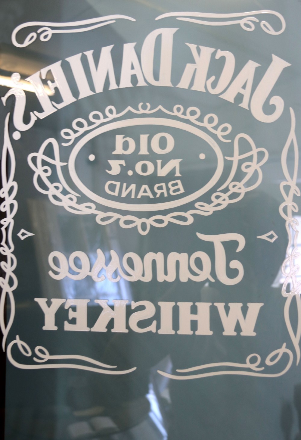 A late Victorian warm brown wooden cabinet featuring a glazed upper display section with white Jack Daniels typography and two lower panelled doors. View XV