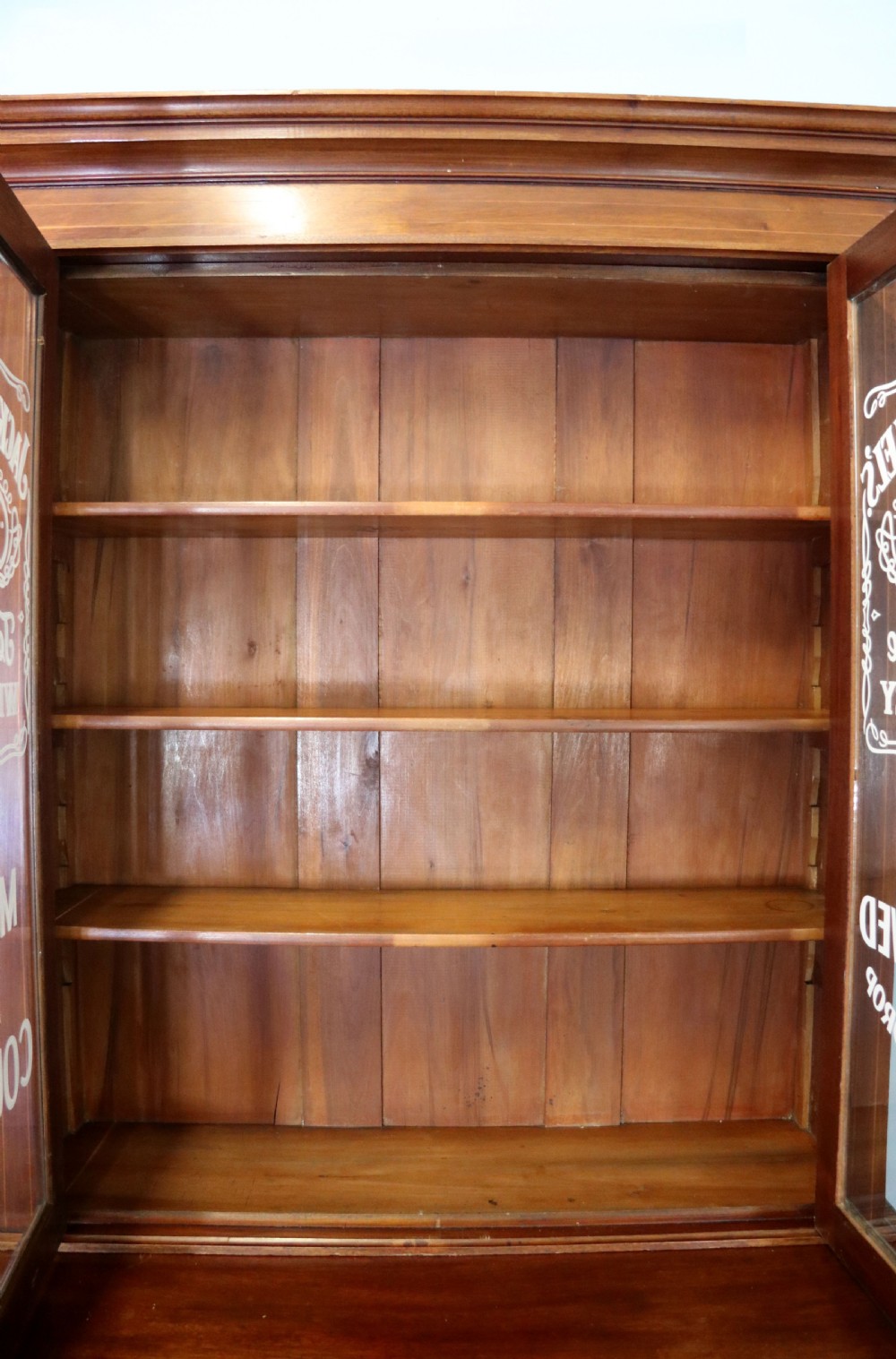 A late Victorian warm brown wooden cabinet featuring a glazed upper display section with white Jack Daniels typography and two lower panelled doors. View XVII