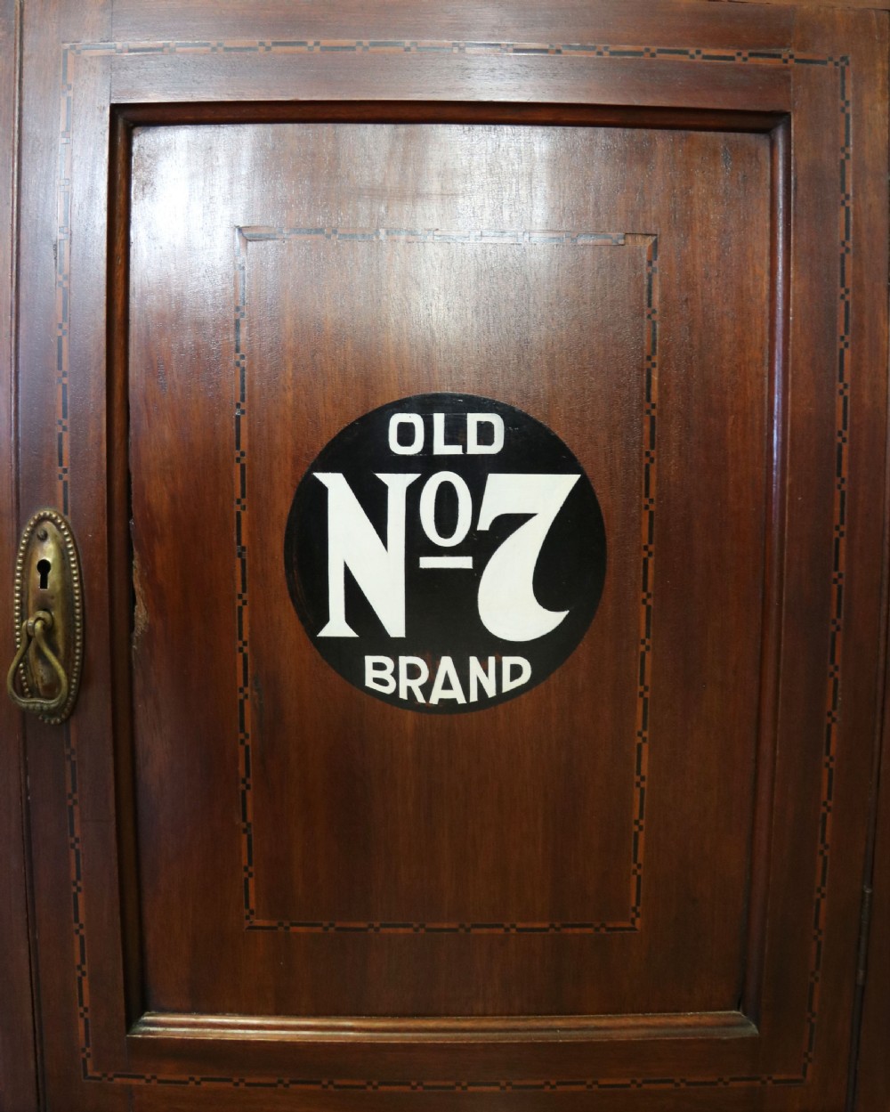 A late Victorian warm brown wooden cabinet featuring a glazed upper display section with white Jack Daniels typography and two lower panelled doors. View XXIV