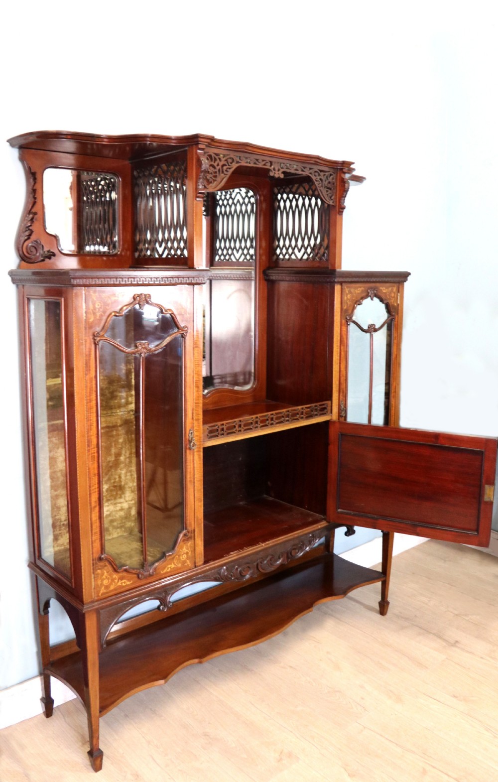 A late 19th-century mahogany display cabinet featuring a drop-centre mirror back, detailed floral marquetry inlays, glazed side doors, and a lower open shelf. View V