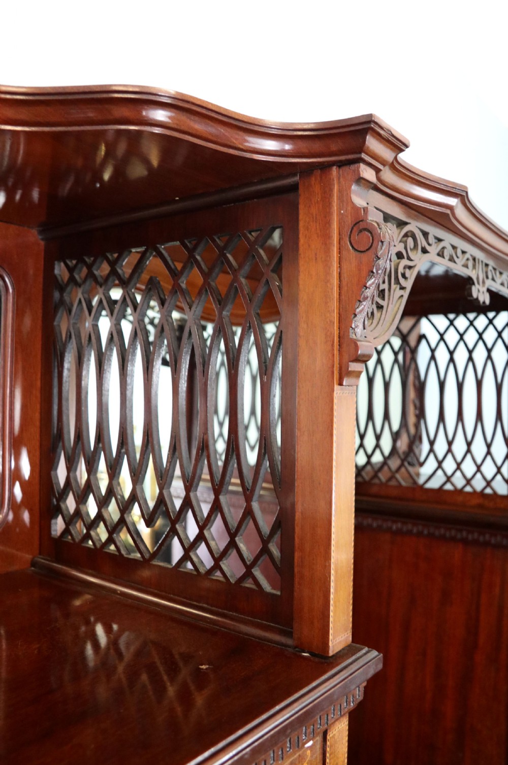 A late 19th-century mahogany display cabinet featuring a drop-centre mirror back, detailed floral marquetry inlays, glazed side doors, and a lower open shelf. View VII