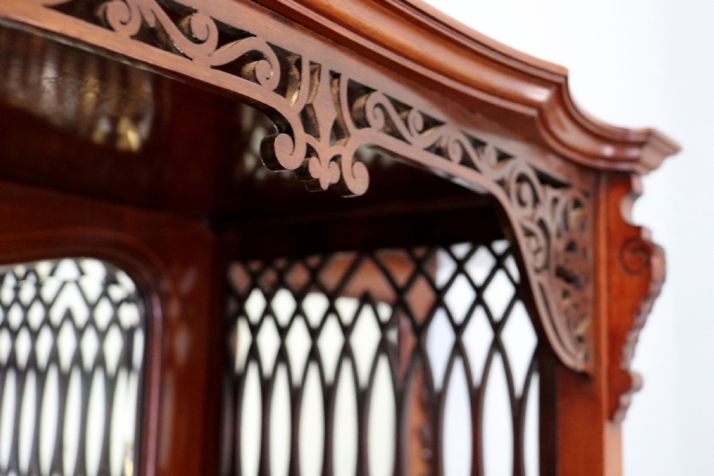 A late 19th-century mahogany display cabinet featuring a drop-centre mirror back, detailed floral marquetry inlays, glazed side doors, and a lower open shelf. View VIII