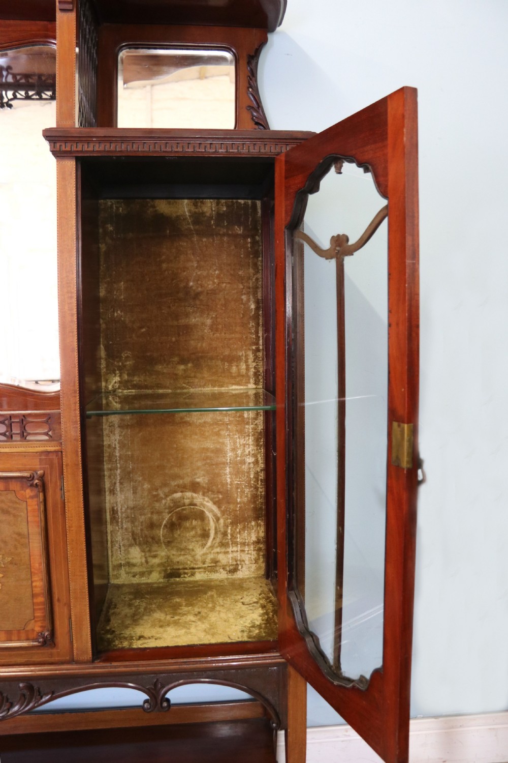 A late 19th-century mahogany display cabinet featuring a drop-centre mirror back, detailed floral marquetry inlays, glazed side doors, and a lower open shelf. View XI