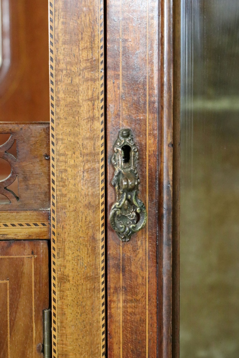 A late 19th-century mahogany display cabinet featuring a drop-centre mirror back, detailed floral marquetry inlays, glazed side doors, and a lower open shelf. View XIII