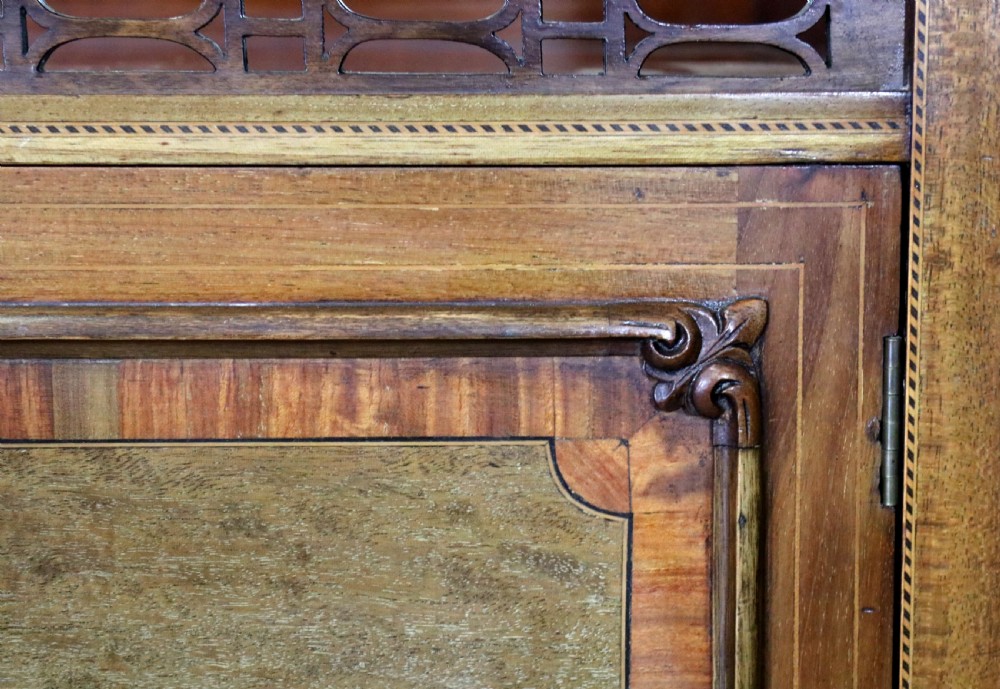 A late 19th-century mahogany display cabinet featuring a drop-centre mirror back, detailed floral marquetry inlays, glazed side doors, and a lower open shelf. View XVII