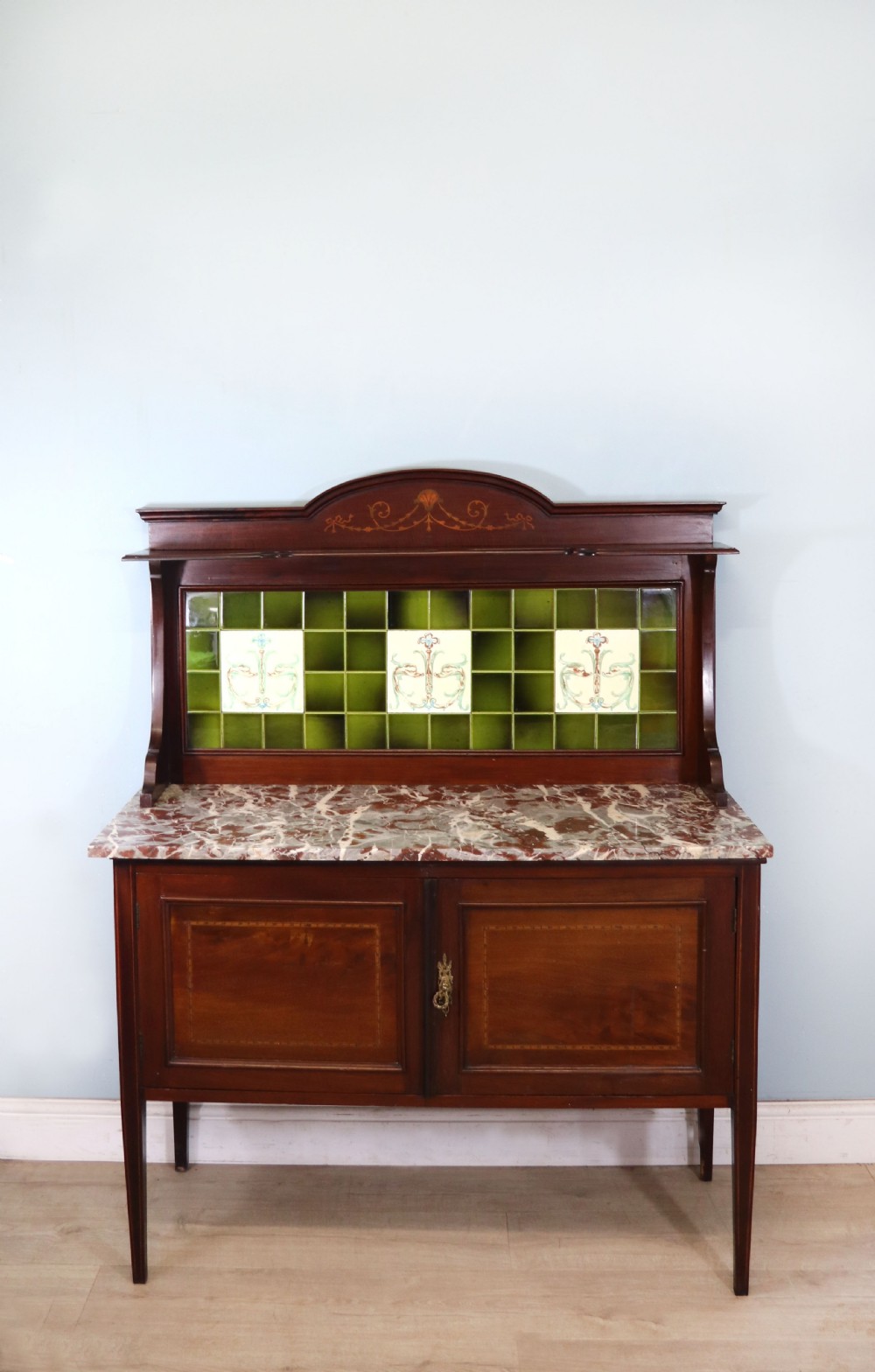 An Edwardian mahogany washstand featuring a red variegated marble top, a splashback set with green ceramic tiles, inlaid cupboard doors, and tapered legs. View II
