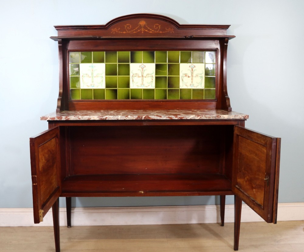 An Edwardian mahogany washstand featuring a red variegated marble top, a splashback set with green ceramic tiles, inlaid cupboard doors, and tapered legs. View IV