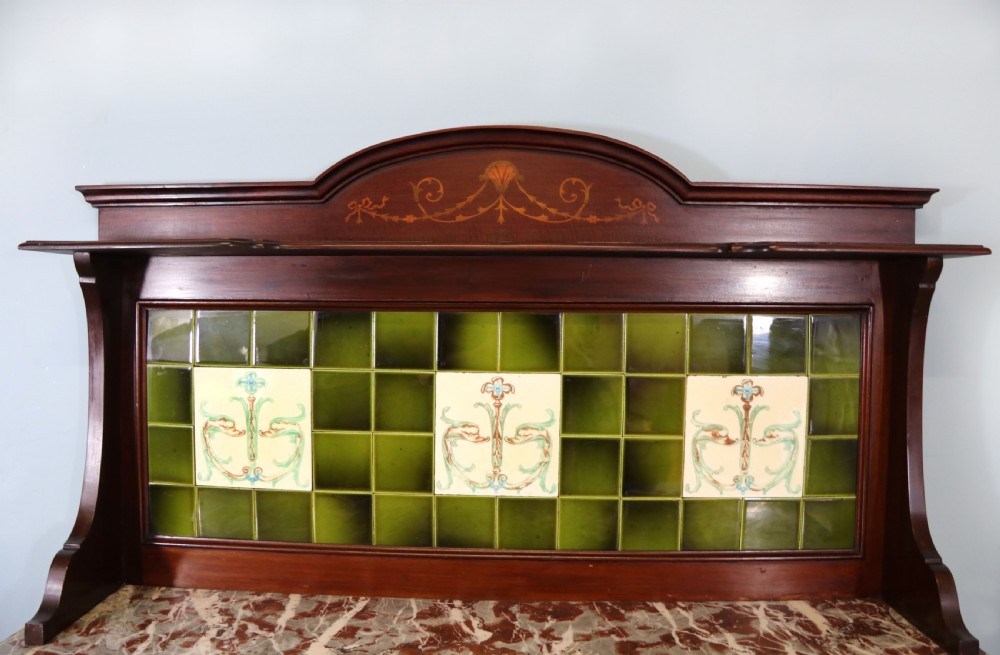 An Edwardian mahogany washstand featuring a red variegated marble top, a splashback set with green ceramic tiles, inlaid cupboard doors, and tapered legs. View VI