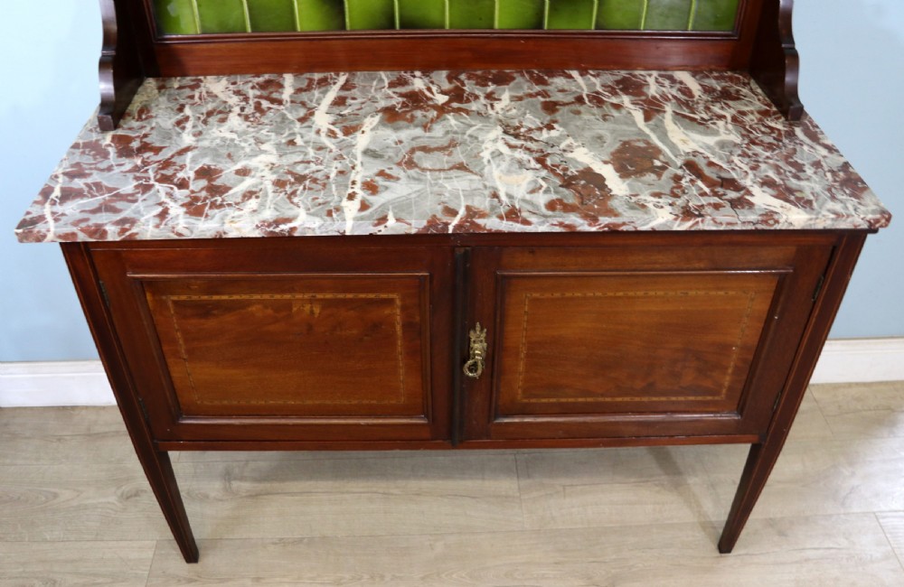 An Edwardian mahogany washstand featuring a red variegated marble top, a splashback set with green ceramic tiles, inlaid cupboard doors, and tapered legs. View XIV