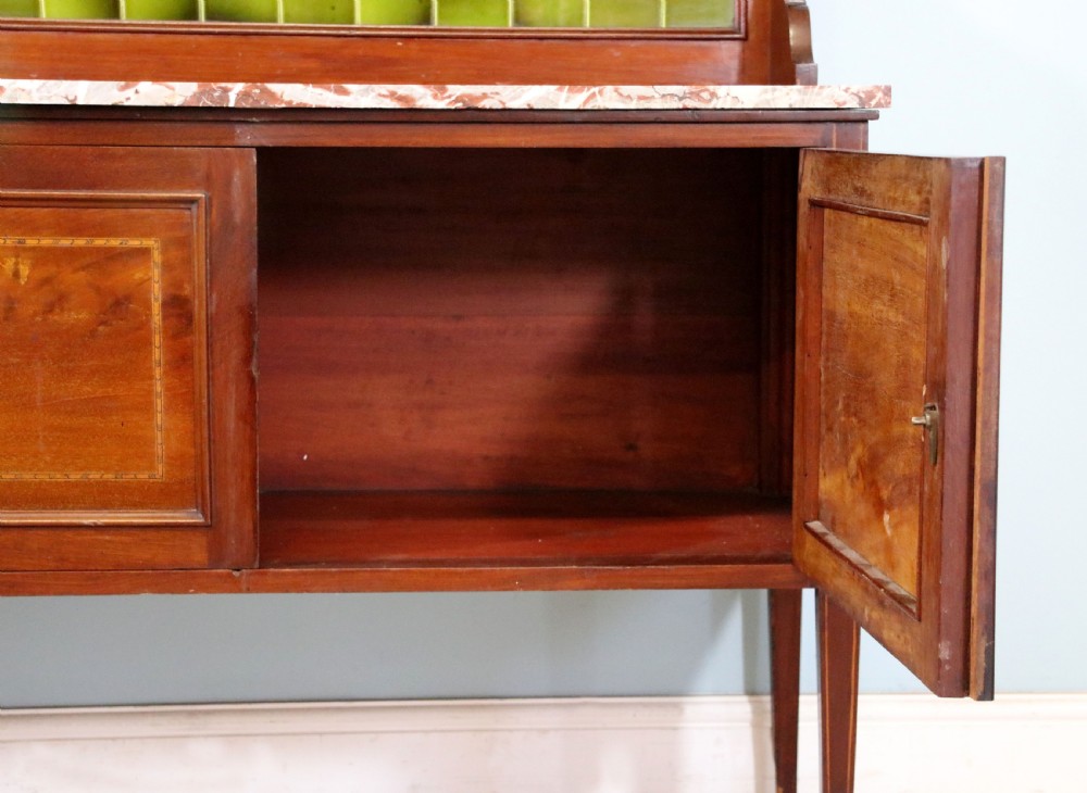 An Edwardian mahogany washstand featuring a red variegated marble top, a splashback set with green ceramic tiles, inlaid cupboard doors, and tapered legs. View XVIII