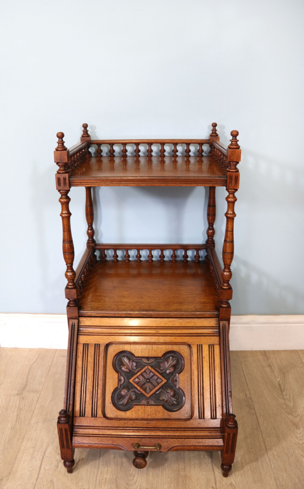 A Victorian Gothic Revival solid walnut coal purdonium featuring a carved drop-front compartment, turned spindle galleries, and upper open shelves.
