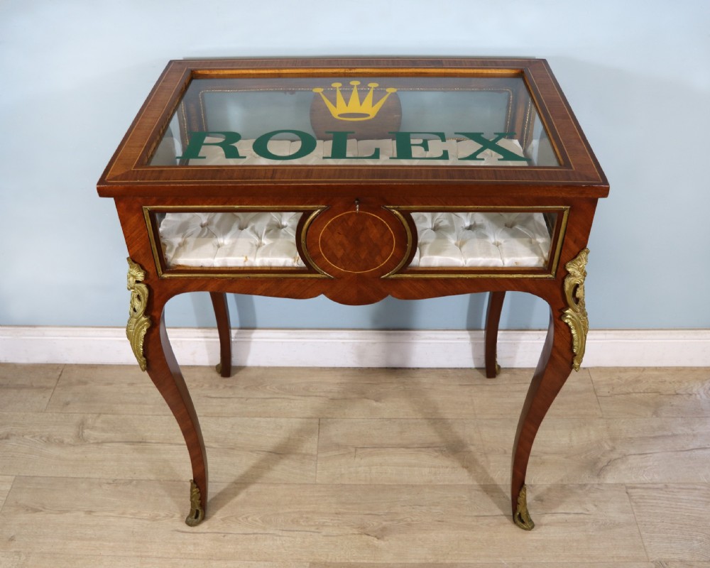 A mahogany and kingwood veneered bijouterie display table featuring glazed panels, cabriole legs with brass mounts, and a buttoned cream interior.