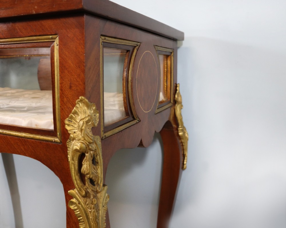 A mahogany and kingwood veneered bijouterie display table featuring glazed panels, cabriole legs with brass mounts, and a buttoned cream interior. View X