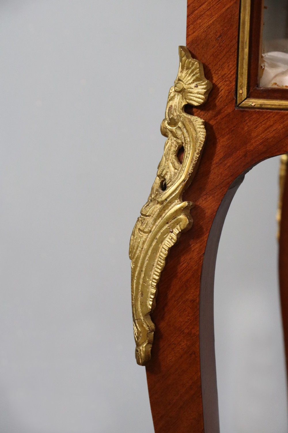 A mahogany and kingwood veneered bijouterie display table featuring glazed panels, cabriole legs with brass mounts, and a buttoned cream interior. View XXIV