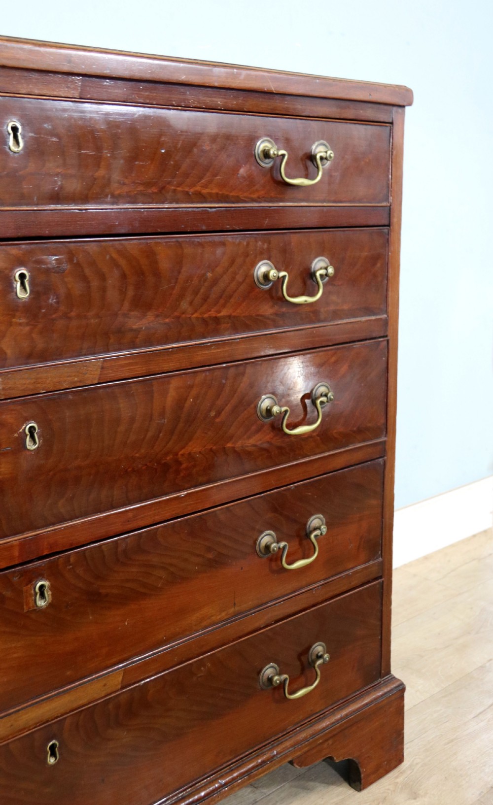 A 19th-century mahogany chest of drawers featuring five graduated drawers with brass swan-neck handles and bracket feet. View IX